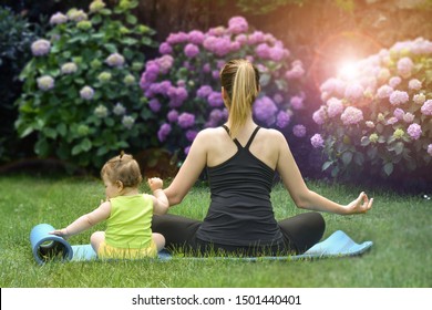 Young Sports Mother Doing Physics Exercise Outdoors In Garden Near Her Cute Adorable Baby Daughter. Healthy Lifestyle. Yoga. Fitness. Family Having Fun Outside. Family Spend Time Together In Park.