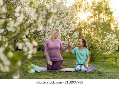 Young Sports Mother Doing Physics Exercise Outdoors In Garden Near Her Daughter. Healthy Lifestyle. Yoga. Fitness. Family Having Fun Outside. Family Spend Time Together In Park.