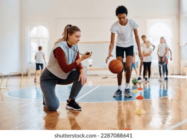 Young sports teacher measuring time on stopwatch during PE class with elementary students at school gym. - Powered by Shutterstock