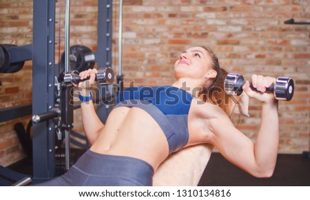 Young sports woman doing exercises with dumbbells in gym