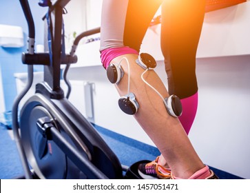 Young Sports Woman With Electrostimulator On The Muscles Of The Legs. Fitness Training With An Electrostimulator. Physiotherapy.