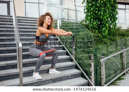 Young sports woman having a break near the gray wall on the stairs after morning jogging in the modern city. Healthy lifestyle in the city.