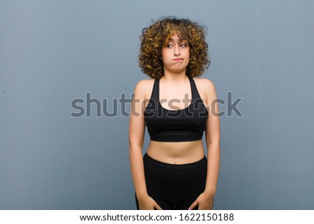 young sports woman wondering, thinking happy thoughts and ideas, daydreaming, looking to copy space on side against gray wall