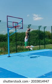 Young sportsman with basketball ball jumping under hoop on playground