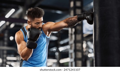 Young sportsman boxing workout at gym, guy punching boxing bag, free space