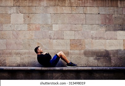 Young sportsman doing abdominal crunches against brick wall with copy space area for your text message or advertising content, sporty guy engaged an intensive fitness training in urban setting - Powered by Shutterstock