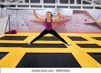 Young sportsman jumping on a trampoline and doing split indoors