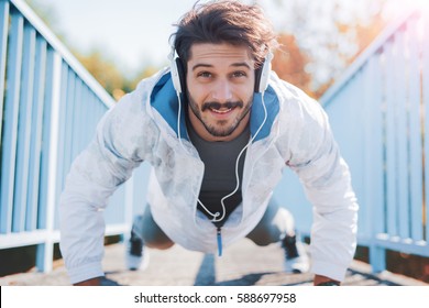 Young sportsman listening to music while doing push ups outdoors, fitness and exercising in the park. Fitness, sport, lifestyle concept - Powered by Shutterstock