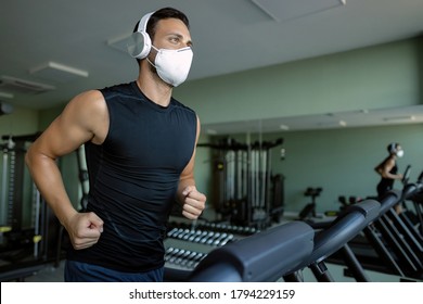 Young Sportsman Wearing A Face Mask While Running On Treadmill At Health Club During Coronavirus Epidemic. 