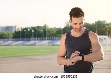 Young Sportsman With Wireless Earphones And Smart Watch At Stadium