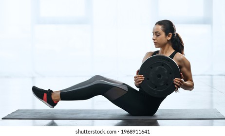young sportswoman doing abs with weight plate on fitness mat in gym
