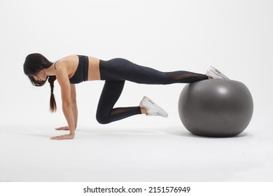 young sportswoman doing basic plank exercise with fitness ball isolated on white background