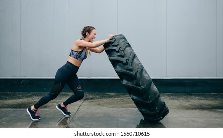 Young sportswoman doing cross-training lifting a tire on a rainy day - Powered by Shutterstock