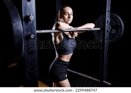 Young sportswoman doing exercises with barbell in the gym. Fitness girl posing with barbell