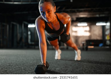 Young sportswoman is doing plank exercises with dumbbells in a modern gym, demonstrating her commitment to a healthy lifestyle - Powered by Shutterstock