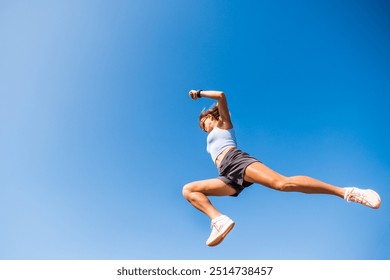 Young sportswoman is jumping a hurdle during a parkour training session against a blue sky - Powered by Shutterstock