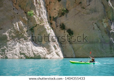 Young sportswoman on kayak with a lot of energy. Amazing views on kayak. Beautiful blue river under amazing rocks. Summer landscape. Perfect activity for holidays. 