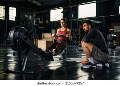 Young sportswoman practicing on rowing machine during sports training with her personal trainer in a gym.  - Powered by Shutterstock