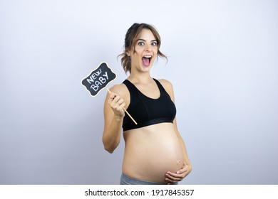 Young Sportswoman Pregnant Wearing Sportswear Over White Background Amazed And Holding Blackboard With New Baby Word Message