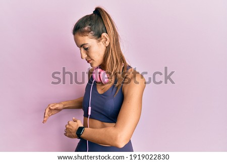 Young sportswoman stretching muscles after doing exercise wearing sporty clothes and headphones, standing doing flexibility activity
