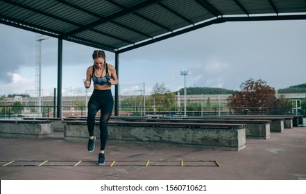 Young Sportswoman Training Jumping On An Agility Ladder Outdoors