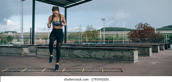 Young Sportswoman Training Jumping On An Agility Ladder Outdoors