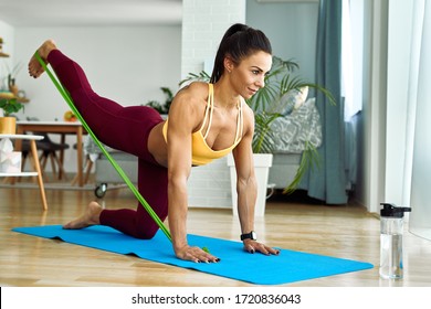 Young Sportswoman Using A Power Band While Doing Leg Exercises At Home. 