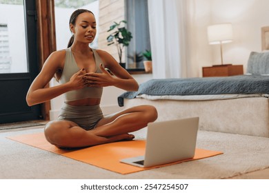 Young sporty African American woman having online yoga meditation, using laptop, sitting on fitness mat at home. Healthy lifestyle, sport concept - Powered by Shutterstock