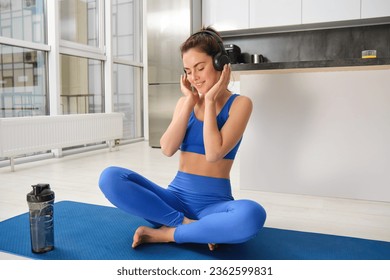 Young sporty athletic fitness trainer instructor woman wear blue tracksuit spend time in home gym use mobile phone headphones listen music. Workout sport concept. - Powered by Shutterstock