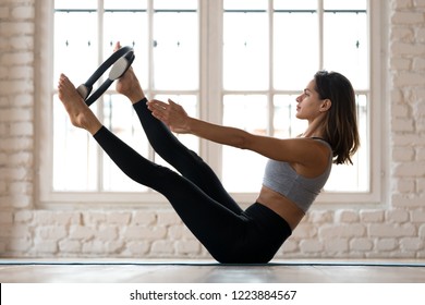 Young sporty attractive woman doing toning pilates exercise for abs and inner thighs with exercise circle, open leg balance with pilates magic circle, indoor full length, at yoga studio or at home - Powered by Shutterstock