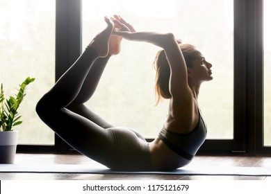 Young sporty attractive woman practicing yoga, doing Dhanurasana exercise, Bow pose, working out, wearing sportswear, grey pants and top, indoor full length, yoga studio. Side view - Powered by Shutterstock