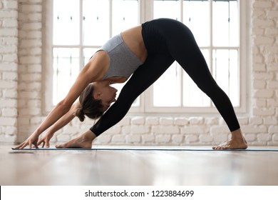 Young sporty attractive woman practicing yoga, doing One Sided Fold exercise, Parsvottanasana, Pyramid pose, working out, wearing sportswear, pants and top, indoor full length, white yoga studio - Powered by Shutterstock