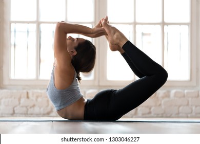 Young sporty attractive woman practicing yoga, doing Dhanurasana exercise, Bow pose, working out, wearing sportswear, black pants and top, indoor full length, yoga studio - Powered by Shutterstock