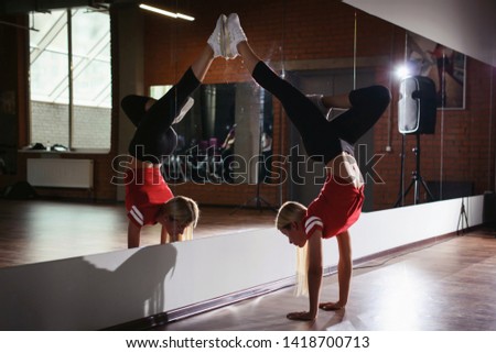 Young sporty attractive woman practicing yoga, doing handstand pose, working out, wearing sportswear, black pants and red top, indoor full length, yoga studio