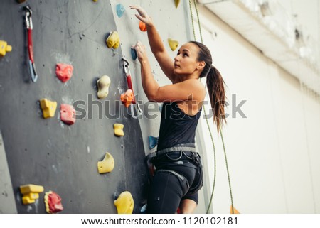 Young sporty caucasian woman practicing rock climbing on artificial wall indoors, side view. Active lifestyle and bouldering concept.