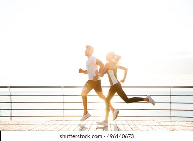 Young Sporty Couple Running Over Wooden Pier At Sunset