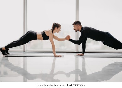 Young sporty couple working out together in a gym . Doing plank exercises while holding each other for one hand. - Powered by Shutterstock