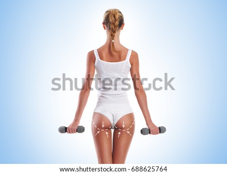 Young, sporty and fit girl with arrows along her buttocks pumping dumbbells over blue background. Sport, fitness and healthy lifestyle concept.