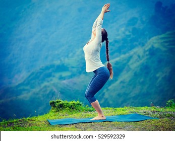 Young sporty fit woman doing yoga asana Utkatasana (chair pose) outdoors in mountains Himalayas in India. Vintage retro effect filtered hipster style image.