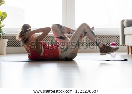 Young sporty fit woman lying on mat floor doing bicycle crunch fitness exercise at home gym, healthy active teen girl training abs workout crisscross cross twist abdominal sit ups alone indoors
