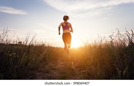 Young Sporty Girl Running On A Rural Road At Sunset In Summer Field. Lifestyle Sports Background  