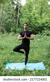 Young Sporty Man In Black Sportswear Doing Yoga And Demonstrating Yoga Tree Pose On The Nature