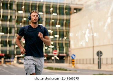 Young sporty man jogging through city streets with backpack on back - Shutterstock ID 2149868595