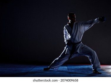Young sporty man in white kimono training karate kata moves in gym