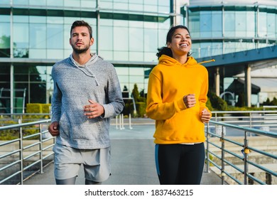 Young Sporty Mixed Race Couple Running Together Against Modern Building Made Of Glass