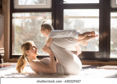 Young sporty mother and baby girl working out, exercising together at home, parent and child healthy development, game playing, fitness and relaxation, wearing white. Healthy lifestyle concept photo 