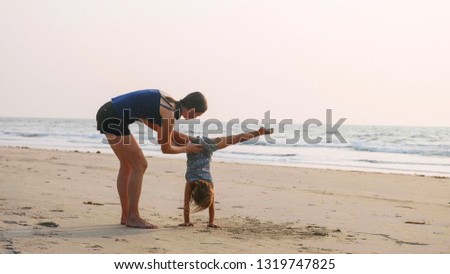 Young sporty mother train little girl doing handstand position.  Mom with little daughter doing gymnastic on the beach. Acrobatic exercise outdoor.