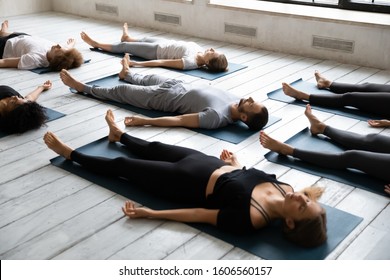 Young sporty people with closed eyes meditating in Savasana pose on floor, practicing yoga at group lesson, doing Corpse exercise on mats, training, working out in modern yoga studio, center - Powered by Shutterstock