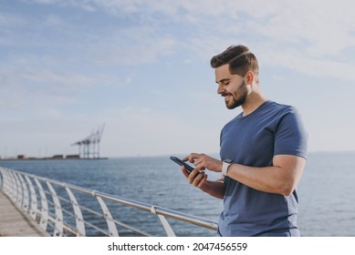 Young sporty smiling fit tourist traveler sportsman man 20s in sports clothes warm up training walking chat by mobile cell phone at sunrise over sea beach outdoor on pier seaside in summer day morning - Powered by Shutterstock