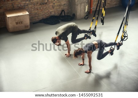 Young and sporty. Top view of a couple in sportswear training with Trx fitness straps at gym